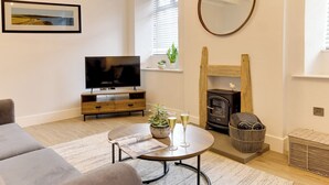 A modern living room with a flat-screen TV, a fireplace, a round coffee table, and a sofa. - Beam End Snainton - Modern 2-bedroom Stone Cottage. Pet Friendly. (Snainton)