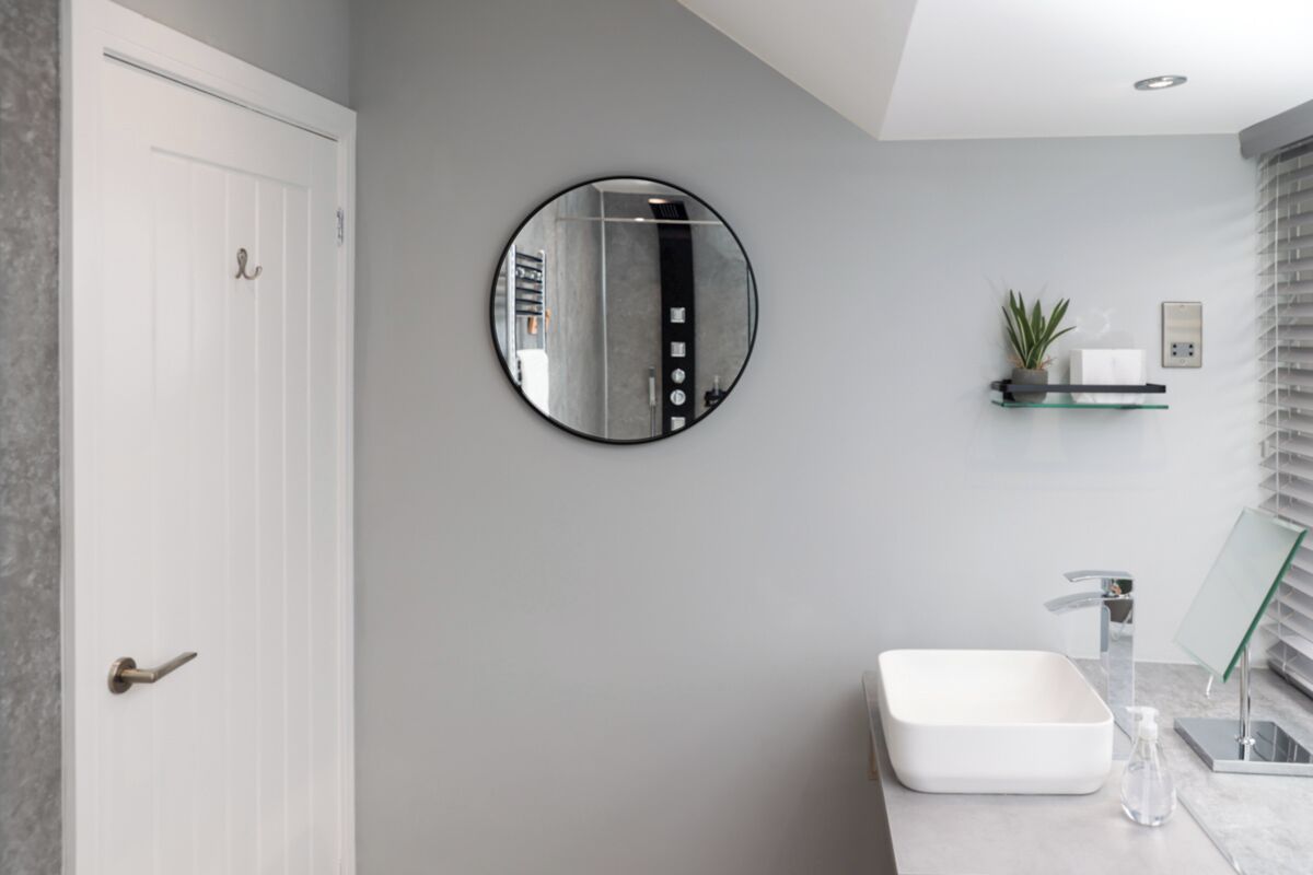 Een moderne badkamer met een witte deur, een ronde spiegel, een rechthoekig wastafelmeubel en een glazen plankje met een plant.