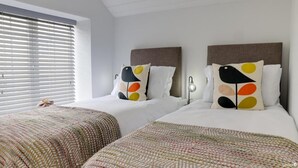 A hotel room with two beds, each with a unique pillow design, a bedside lamp, and a woven throw blanket. - Beam End Snainton - Modern 2-bedroom Stone Cottage. Pet Friendly. (Snainton)