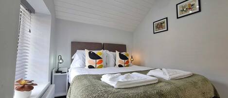 A neatly made bed with white linens and colorful pillows, a bedside lamp, and a folded towel on the floor.