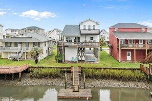Een pand aan het water met een aanlegsteiger, een twee verdiepingen tellend huis met een balkon, en een rood gebouw.