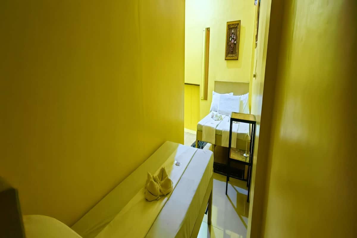 Habitació petita amb un llit individual, una taula de nit i una prestatgeria penjada a la paret.