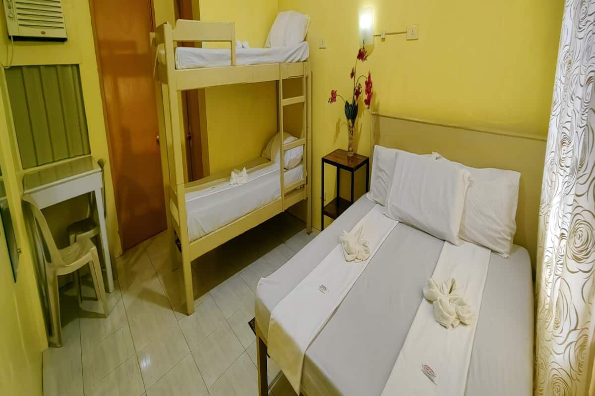 Una habitació amb un llit superposat, un llit individual, una taula petita amb un ram de flors i una cadira.