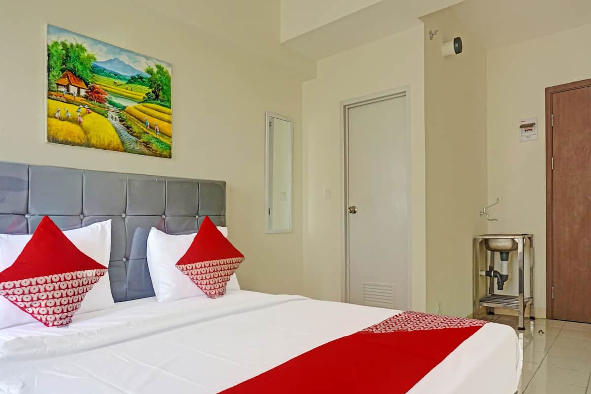 Une chambre d’hôtel avec un lit, un tableau, une porte et un petit lavabo.