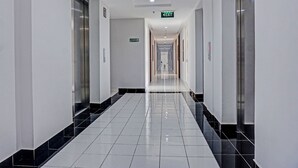 Ein langer, schmaler Gang mit glänzendem Fliesenboden, Türen an beiden Seiten und einem Ausgangsschild am Ende.