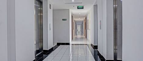 Un pasillo largo y estrecho con suelo de baldosas brillantes, puertas a ambos lados y una señal de salida al final.