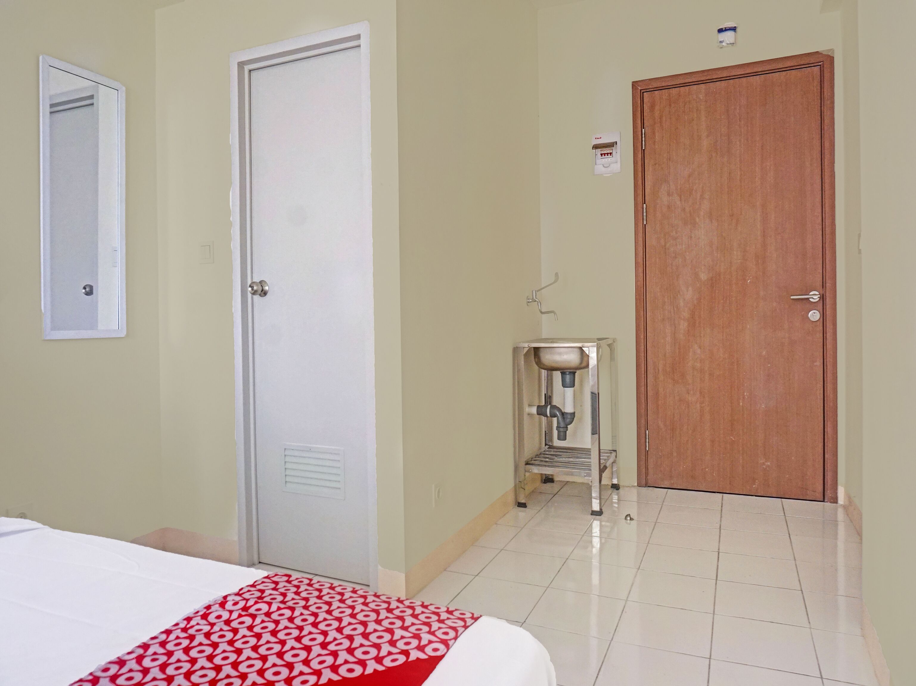 A hotel room with a bed, a wooden door, a small sink, and a mirror on the wall.