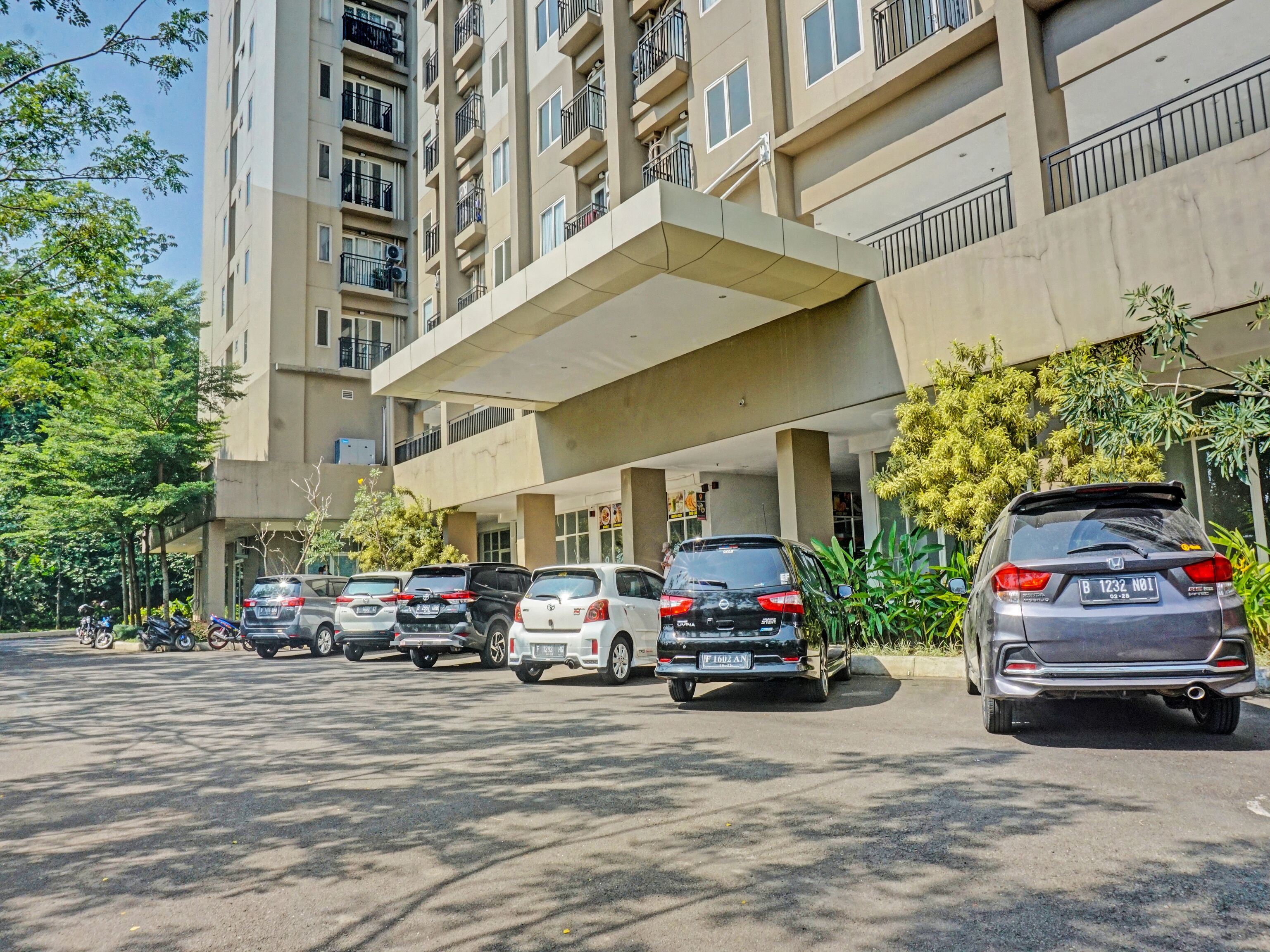 A multi-story parking structure with several cars parked, surrounded by trees and a building with balconies.