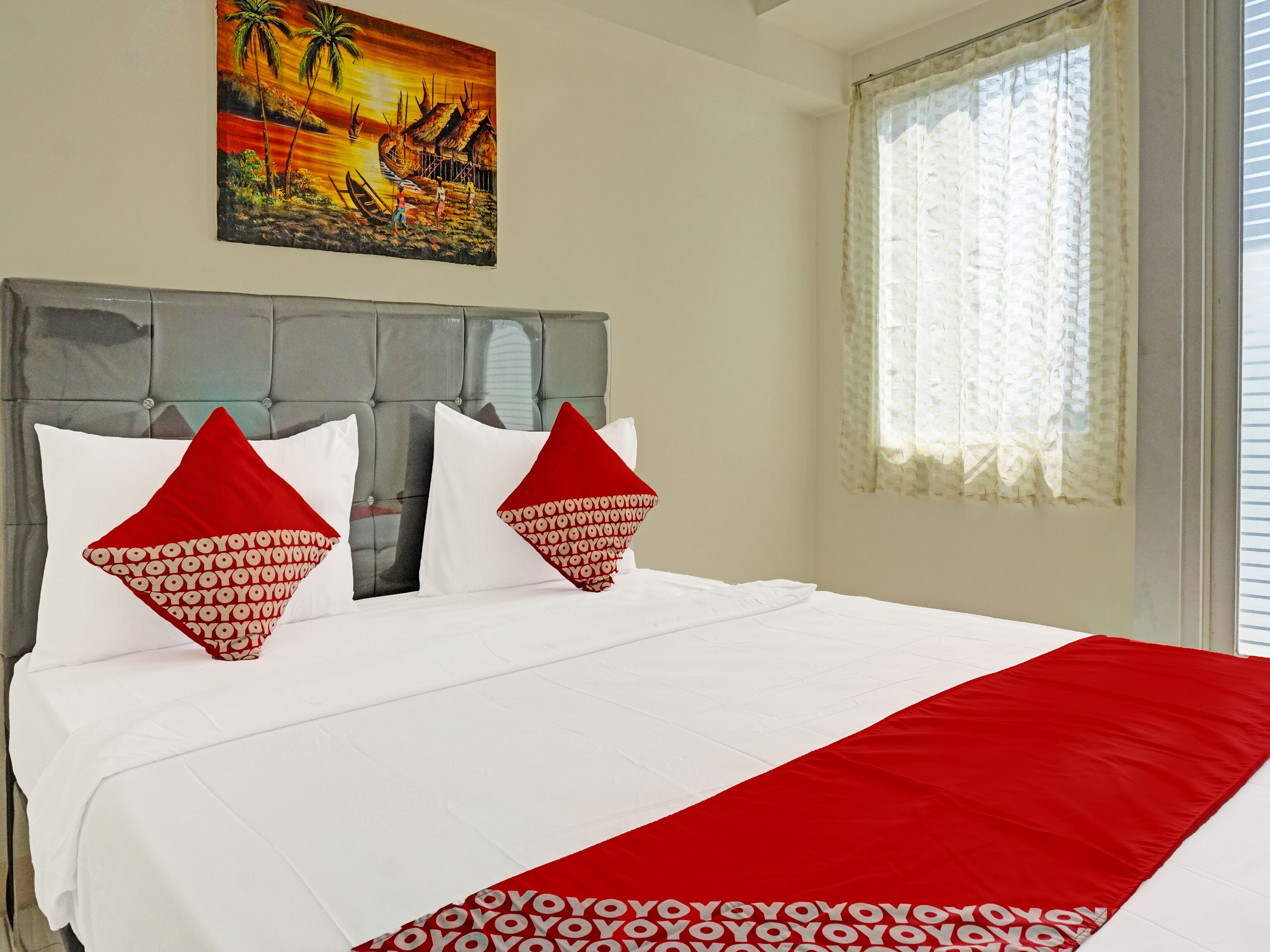 A hotel room with a bed, a painting on the wall, and a window with curtains.