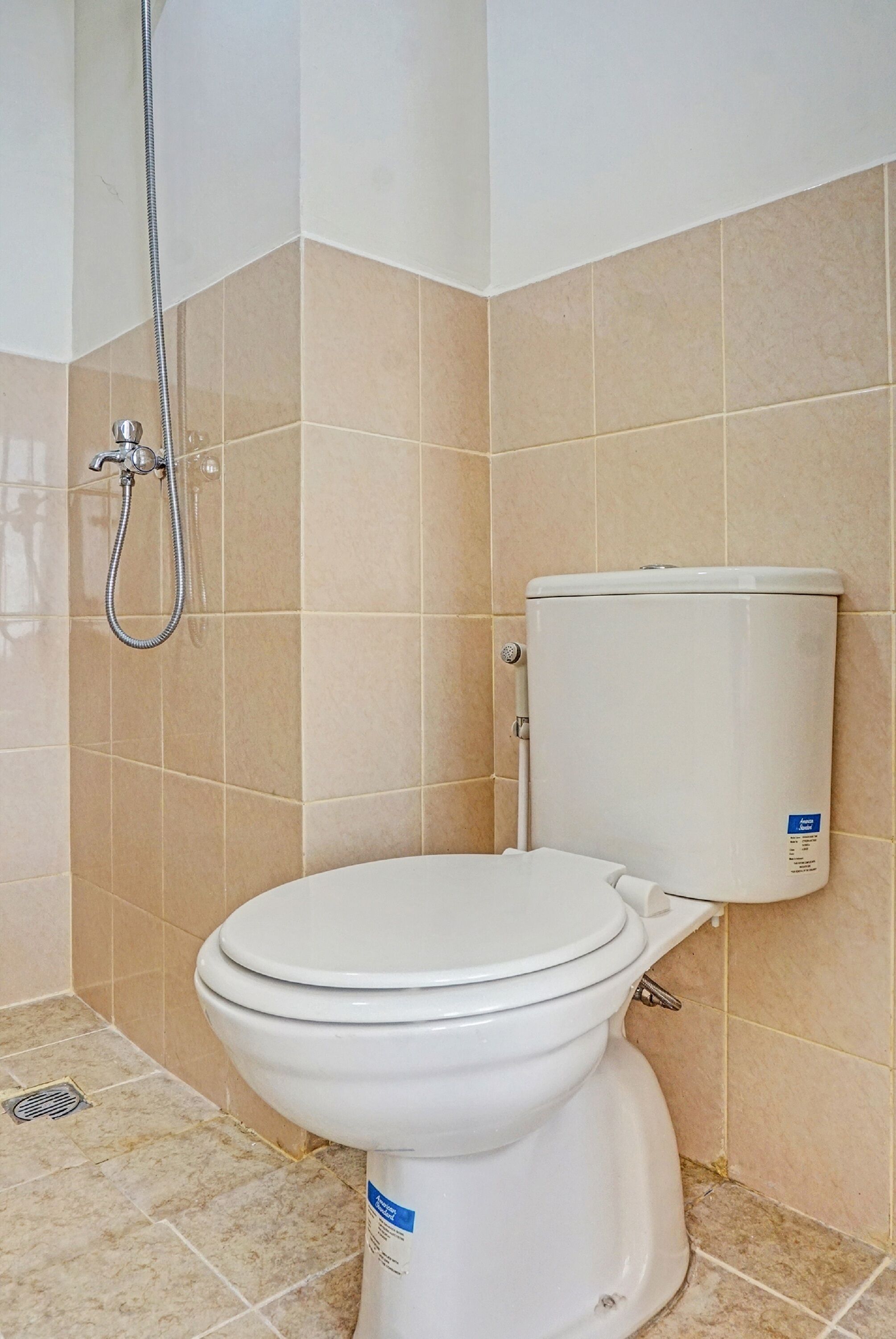 A bathroom with a white toilet, beige tiles, and a showerhead.