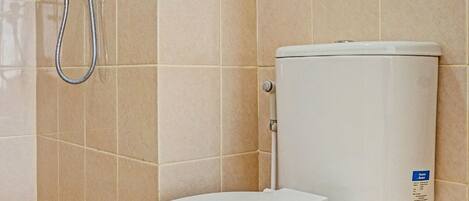 A bathroom with a white toilet, beige tiles, and a showerhead.