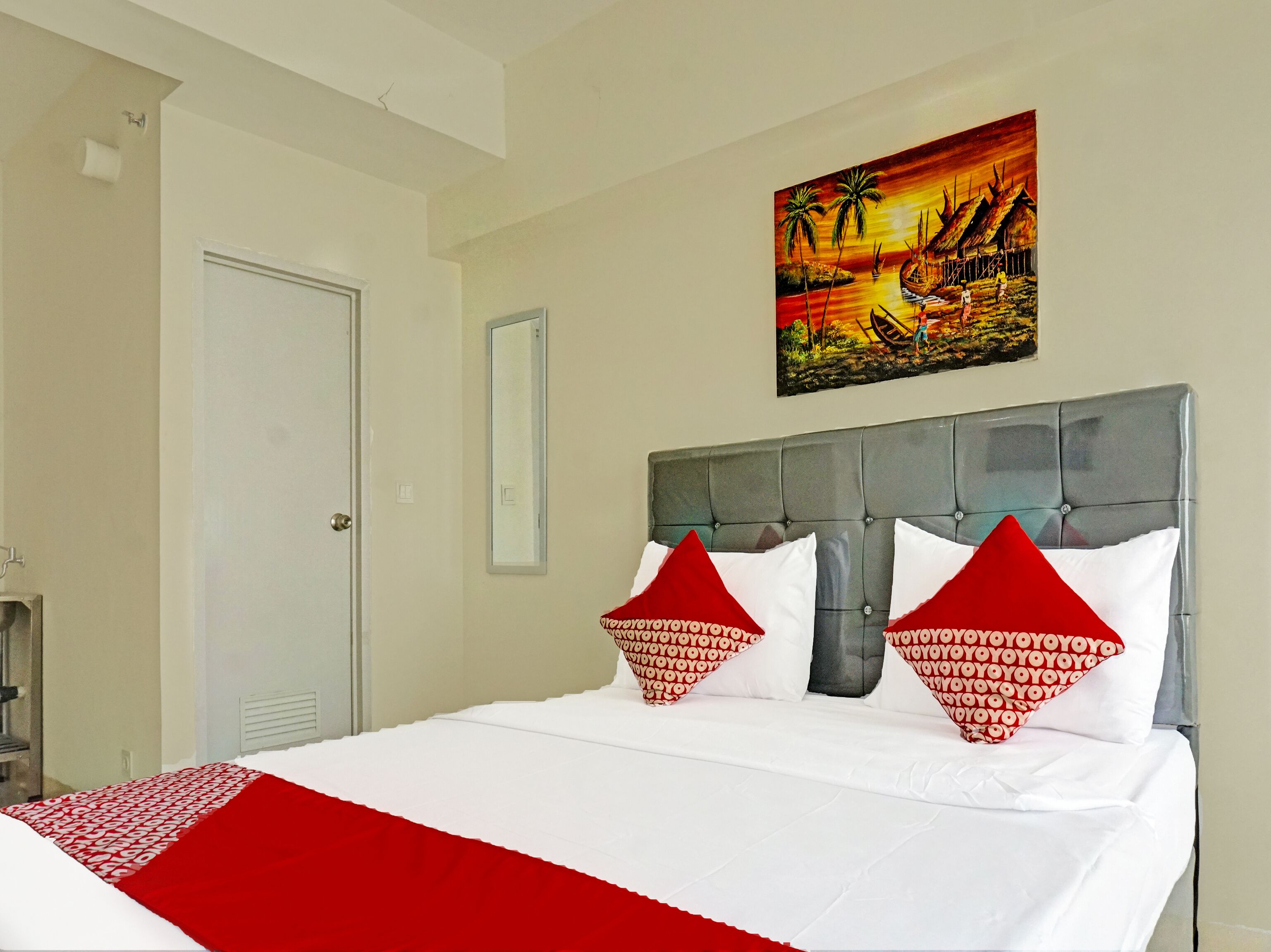 A hotel room with a bed, a painting of a sunset scene, and a door.