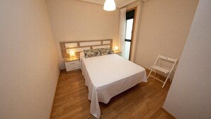 Een slaapkamer met een houten bed, nachtkastjes met lampen, een witte stoel en een raam met gordijnen.