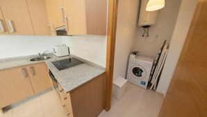 Een compacte keuken met een ingebouwde magnetron, een spoelbak en een fornuis. Er staat een wasmachine en een wasmand in de hoek.