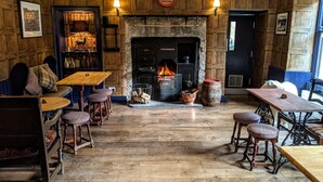 A cozy pub with a stone fireplace, wooden furniture, and a bookshelf. - The White Hart Inn (Hawes)