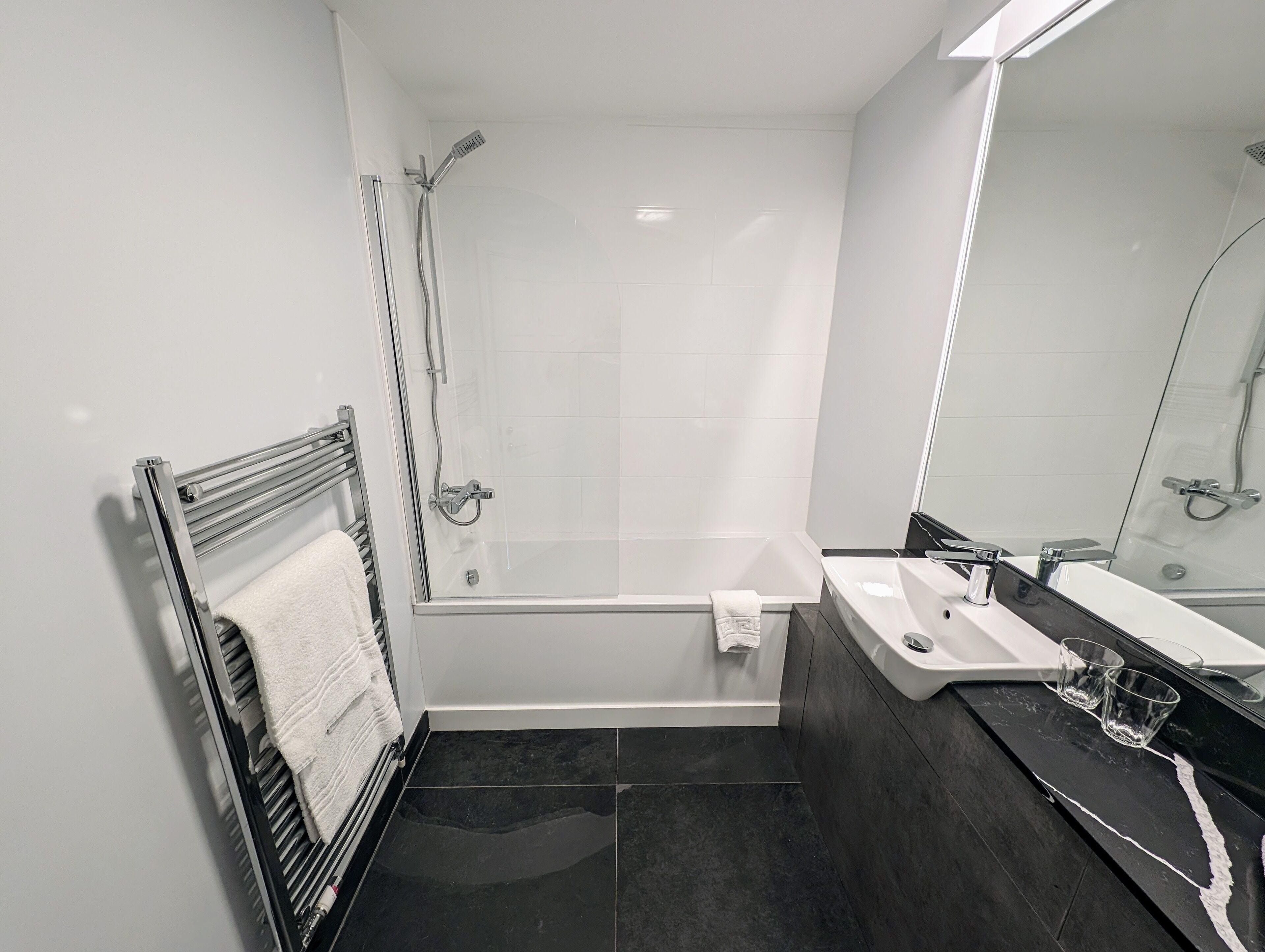 A modern bathroom with a glass-enclosed shower, a bathtub, and a vanity with a sink and mirror.