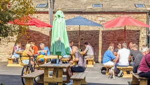 An outdoor seating area with wooden tables and benches, covered by umbrellas, and a stone building in the background. - The White Hart Inn (Hawes)