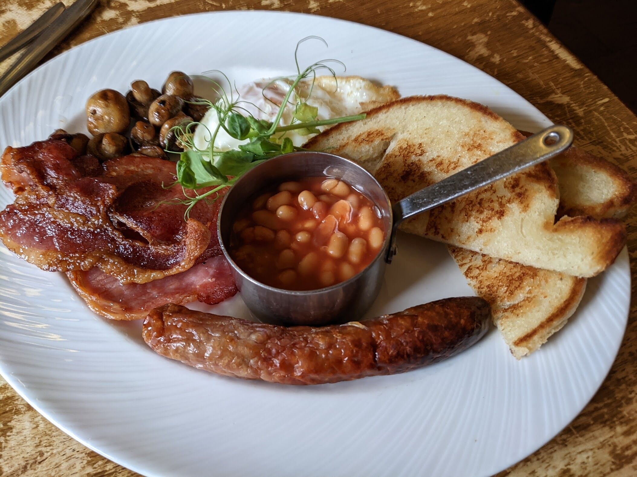 Un plato con tocino, salchichas, frijoles, tostadas y champiñones.