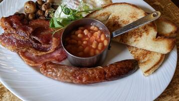 Un plato con tocino, salchichas, frijoles, tostadas y champiñones.
