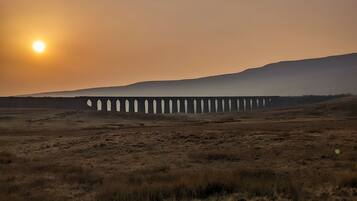 A long bridge in a barren landscape with the sun setting in the background.