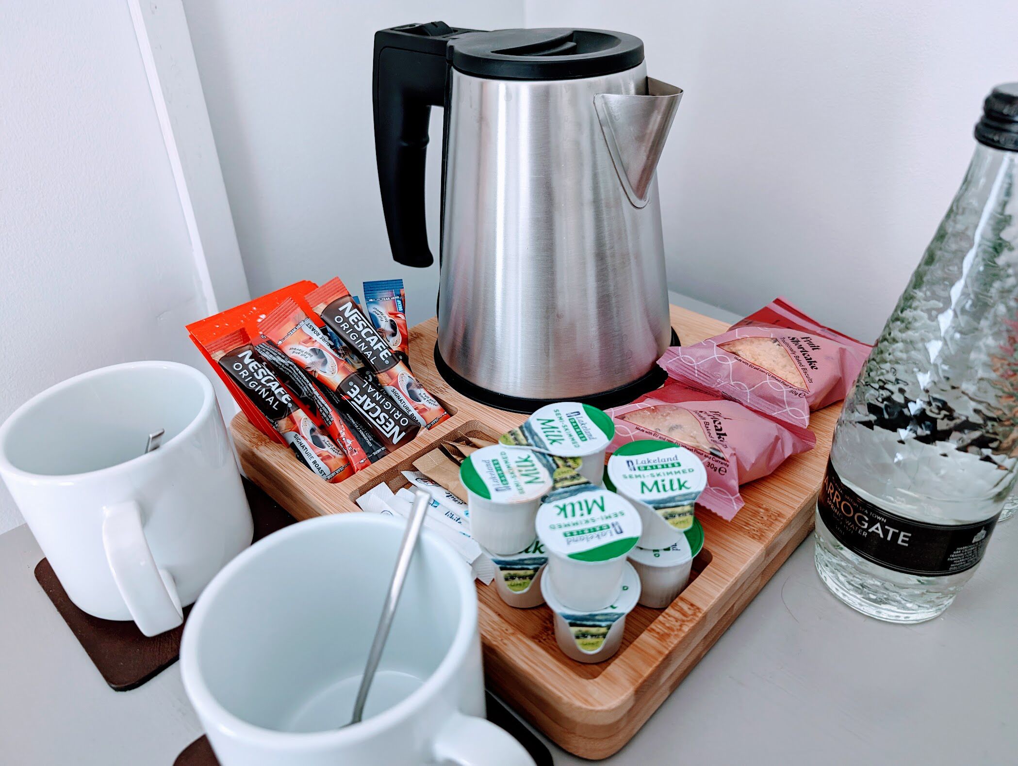 Una preparación para el desayuno con hervidor, sobres de café, cartones de leche y una botella de agua.