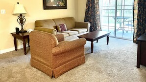 A living room with a sofa, armchair, coffee table, lamp, and a painting on the wall.