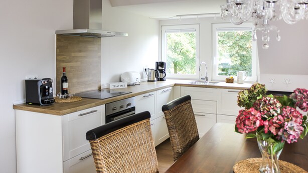 A modern kitchen with white cabinetry, a wooden countertop, and a dining area with wicker chairs and a wooden table. - Deichkind * Holiday apartment on the North Sea in Husum * At home by the sea (Husum)