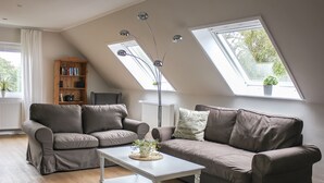 A modern living room with a brown sofa, a white coffee table, and a wooden bookshelf. There are skylights allowing natural light. - Deichkind * Holiday apartment on the North Sea in Husum * At home by the sea (Husum)