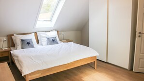 A bedroom with a wooden bed, white bedding, a skylight, a nightstand, and a wardrobe. - Deichkind * Holiday apartment on the North Sea in Husum * At home by the sea (Husum)