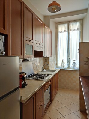 A kitchen with wooden cabinets, a gas stove, a microwave, and a sink. - Stay in the heart of Rome (Roma)