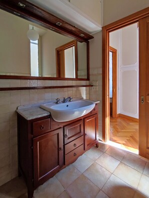 A bathroom with a wooden vanity, a white sink, and a large mirror. - Stay in the heart of Rome (Roma)