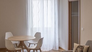 A modern living room with a round dining table, white chairs, a grey sofa, and a large window with sheer curtains. - Stay in the heart of Rome (Roma)