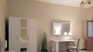 A hotel room with a bed, a desk, a chair, a mirror, and a potted plant. - Stay in the heart of Rome (Roma)