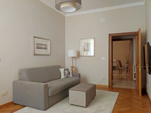 A modern living room with a grey sofa, a small ottoman, a standing lamp, and two framed pictures on the wall. - Stay in the heart of Rome (Roma)