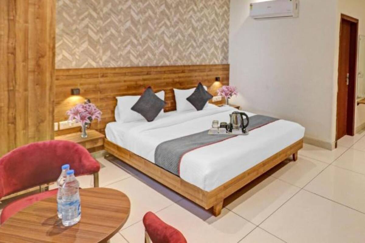 A hotel room with a wooden headboard, a bed with pillows, a bedside table with a lamp, a small table with a water bottle, and a ceiling fan.
