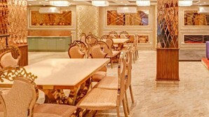 A spacious dining area with high ceilings, ornate chandeliers, and a long table with chairs. - Hotel Golden Glory (New Delhi)