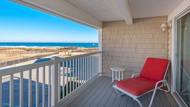 A covered balcony with a red lounge chair, a small table, and a view of the beach and ocean. - Beautiful townhouse with outdoor pool  Free WiFi, linens included and right at the beach. (Ocean City)