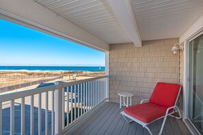 Ein überdachter Balkon mit Liegestuhl in Rot, einem kleinen Tisch und Blick auf Strand und Meer.
