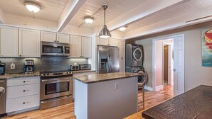 A modern kitchen with stainless steel appliances, a central island, and a dining area with a wooden table. - Beautiful townhouse with outdoor pool  Free WiFi, linens included and right at the beach. (Ocean City)