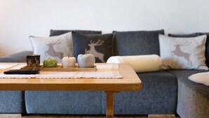 A wooden coffee table with a lace table runner, a remote control, green apples, and candles.