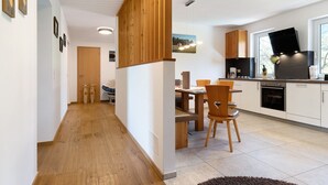 A modern kitchen with wooden cabinets, a dining area with a table and chairs, and a hallway with wooden flooring.