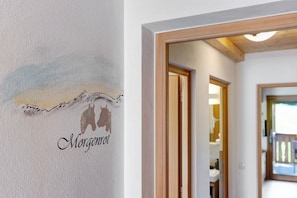 Un couloir avec un chambranle de porte en bois, une enseigne fixée au mur représentant la silhouette d’une montagne et le mot « Morgenrot », et un aperçu d’une pièce avec une fenêtre.