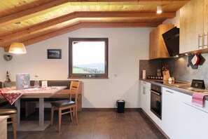 Eine Küche mit Holzausstattung, einem Fenster mit Aussicht, einem Esstisch mit Stühlen und einer kleinen Mülltonne.