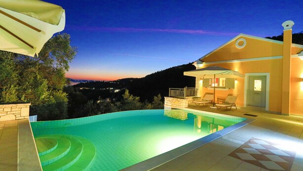 A swimming pool with a stone border, a lounge area with chairs, and a building with a balcony. - Villa Kalamia in Kalami (Corfu)