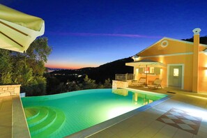 A swimming pool with a stone border, a lounge area with chairs, and a building with a balcony. - Villa Kalamia in Kalami (Corfu)