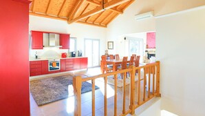 A spacious kitchen with red cabinets, a dining area with wooden chairs, and a high wooden ceiling. - Villa Kalamia in Kalami (Corfu)