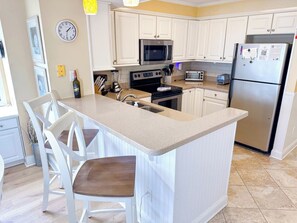 A kitchen with a central island, white cabinetry, a stainless steel refrigerator, and a microwave. - Tilghman Beach and Racquet Club 221 (North Myrtle Beach)