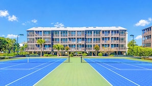 A tennis court with a net, surrounded by a building with multiple balconies and windows.
