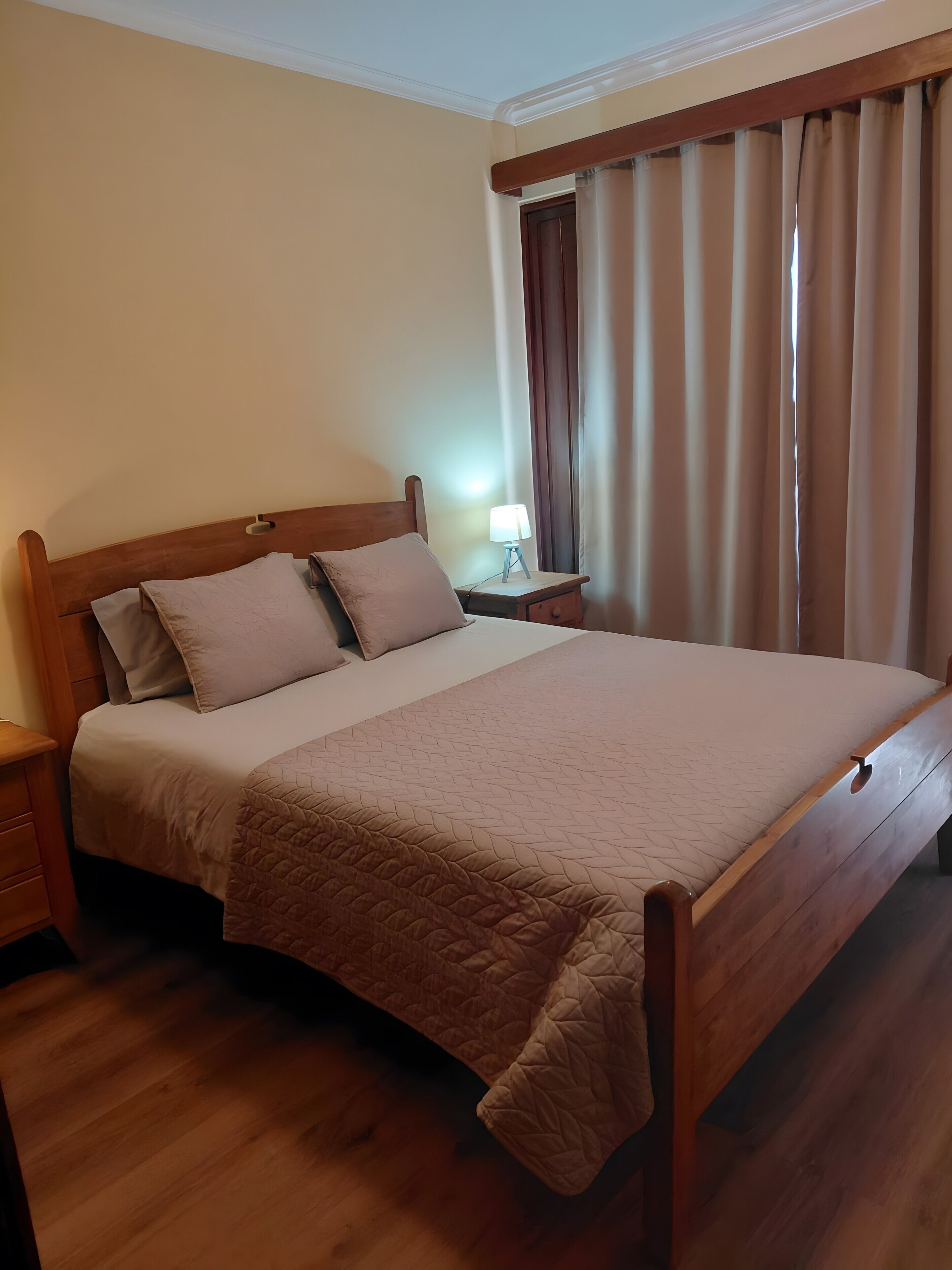 A neatly made bed with a wooden headboard, a bedside lamp, and a window with curtains.