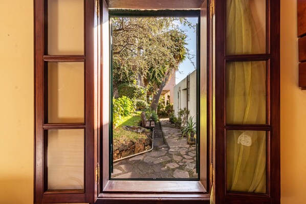 A doorway leading to a stone pathway surrounded by greenery and buildings.